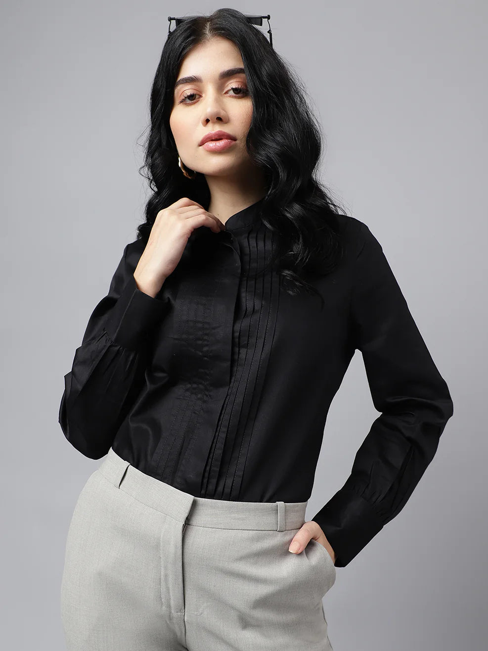Woman wearing a black blouse and light gray pants against a gray background